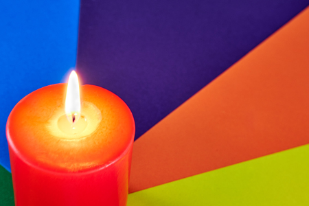 Red wax festive romantic burning candle on a multi-colored background from a color juicy cardboard. love symbol. festive mood. romantic dinner. close upの写真素材