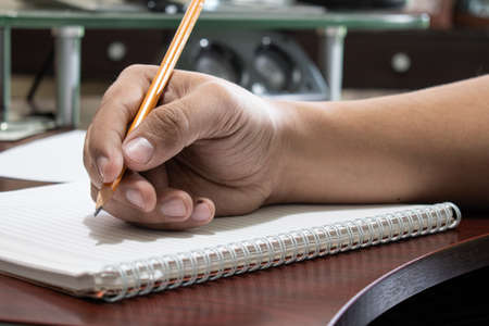 Man's hand holding a pencil over a notebookの写真素材