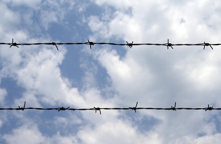 detail of barbed wire fence and deep blue sky and white cloudsの写真素材