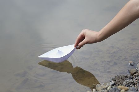 close up ofhand and paper boat in riverの写真素材