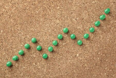 green push pins in shape of finance chart on cork board