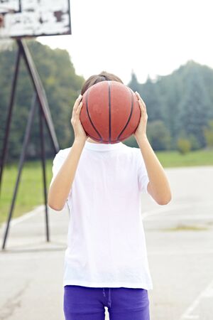 teenage girl holding basket ball in school courtの写真素材
