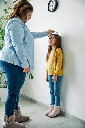 Mother measuring the height of her daughter on the wall at homeの写真素材