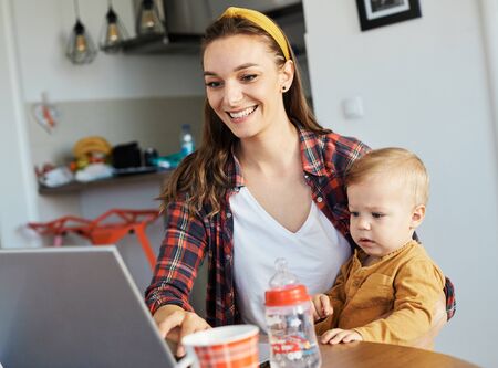 Mother and her baby son working on a laptop together at homeの写真素材