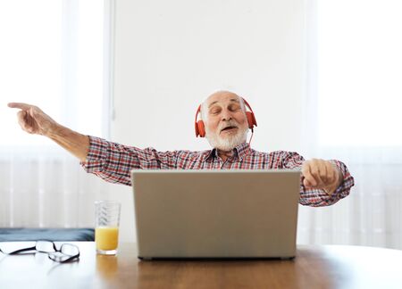 Portrait of an old senior man with headphone  listening to music on a laptop at home