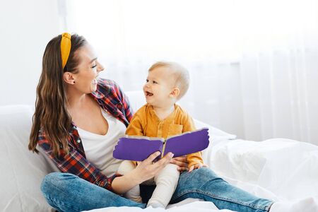 Portrait of a mother and son reading a book and  having fun together at home