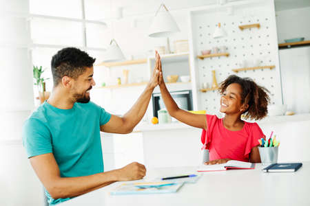 father teaching daughter and helping with homework at home, daughter giving high five to father