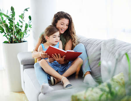 Mother and two sons reading a book on sofa at home