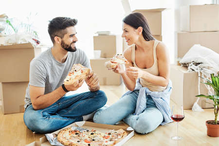 Portrait of a lovely young couple making a break and eating pizza during moving in a new houseの写真素材