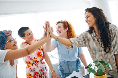 A group of young business women celebrating with high five  in the office or in classroom
