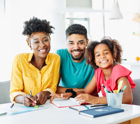 father and mother teaching daughter and helping with homework at homeの写真素材