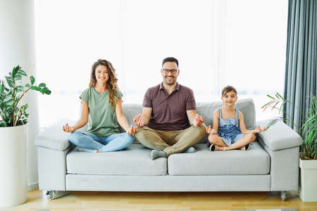 Portrait of a happy young family practicing yoga on sofa at homeの写真素材