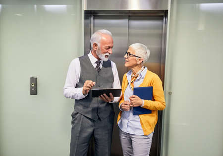 portrait of two senior businesspeople discussing over a tablet in the office