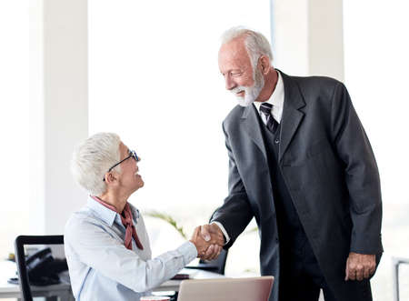 portrait of two senior business people shaking hands introducing each other in the officeの写真素材