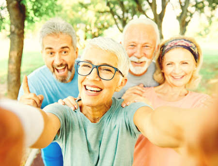 Smiling active senior people posing and taking selfie together in the park