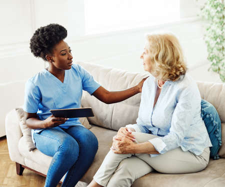 Doctor or nurse caregiver holding a tablet computer with senior woman at home or nursing home
