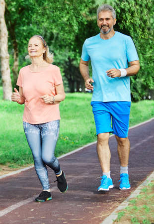 Smiling active senior people jogging together in the park