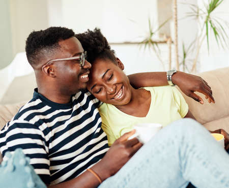 Portrait of a lovely young couple having fun and laughing holding coffee tea cup together at homeの写真素材