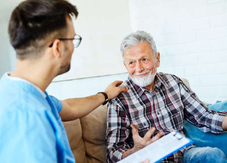 Doctor or nurse caregiver talking with senior man on sofa at home or nursing homeの写真素材