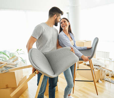 Portrait of a lovely young couple holding chairs moving in a new houseの写真素材