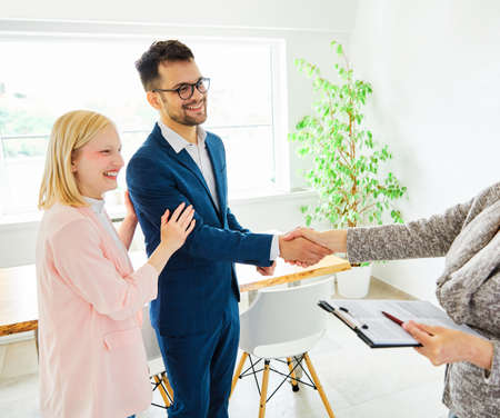 Real estate agent with couple shaking hands closing a deal and signing a contractの写真素材