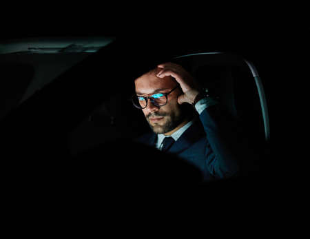 Portrait of a young businessman with tablet or laptop working late at night in office or looking at...
