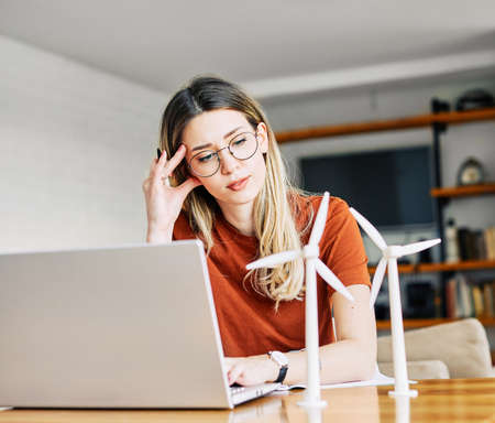 portrait of a young business woman or a student in home office looking at a windmill model and using a laptop computer in the officeの写真素材