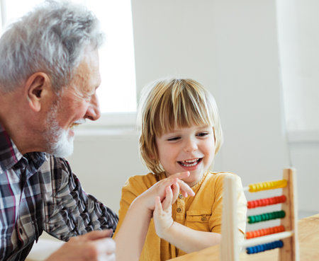 Portrait of grandfather and grandson having fun with an abacus tool or toy doing mathematic calculation and learning together at homeの写真素材