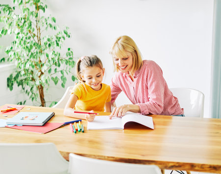mother or teacher teaching daughter and helping her with homework at home or in classroomの写真素材