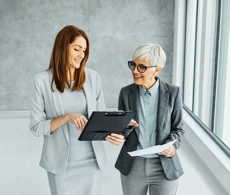 Two young and senior businesswoman walking toghether and having a meeting in the office. Teamwork and success conceptの写真素材