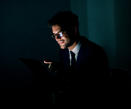 Portrait of a young businessman with tablet or laptop working late at night in officeの写真素材