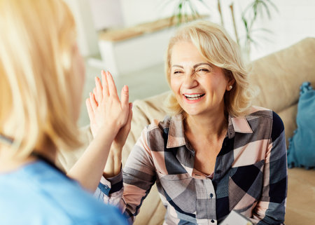 Doctor or nurse caregiver with senior woman giving high five at home or nursing homeの写真素材