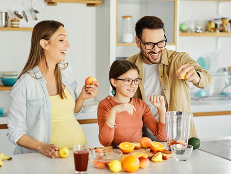 Portrait of a famili with a young pregnant woman preparing a healthy juice with fresh fruits in the kitchenの写真素材