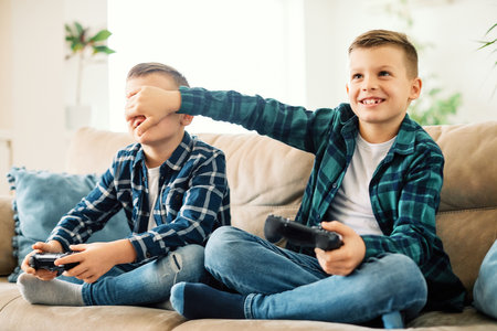 School age brothers laughing and having fun together at home playing games with consoleの写真素材