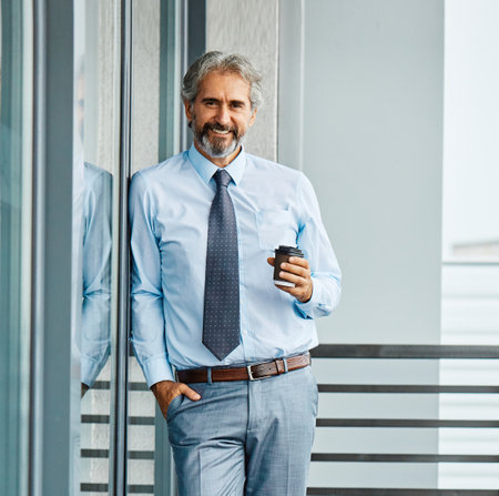 Portrait of a smart inteligent senior businessman holding coffee to go cup in officeの写真素材