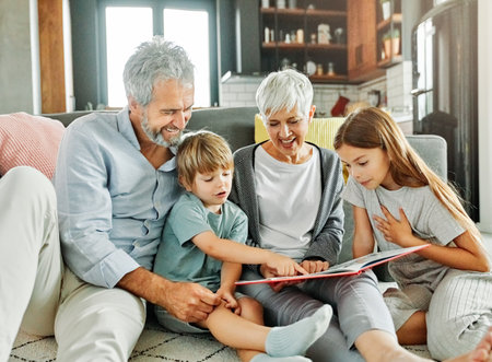 Portrait of grandparents and grandchildren having fun together reading a book at homeの写真素材