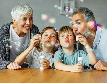 Portrait of grandparents and grandchildren having fun blowing soap bubbles together at homeの写真素材