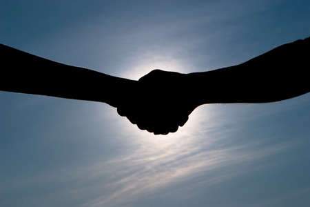 Handshake with covering the sun and clouds and clear sky in background