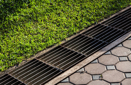 waterway and road - grass. Aqueduct between nature and city. iron grate of water drain in grass garden field. Steel rusty grating in the Grass garden and concrete. Manhole cover metal and way - grass.の写真素材