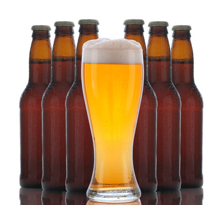 A glass of foamy beer with six brown bottles grouped behind over a white background with reflectionsの写真素材