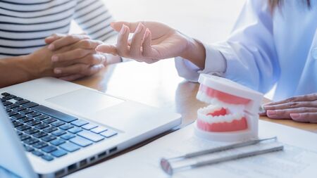 Dentist showing and explaining teeth disease treatment to patient using teeth model denture and...