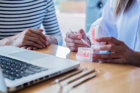 Dentist showing and explaining teeth disease treatment to patient using teeth model denture and explorer mirror tool in dental clinic office. Healthcare concept.の写真素材