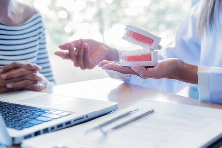 Dentist showing and explaining teeth disease treatment to patient using teeth model denture and explorer mirror tool in dental clinic office. Healthcare concept.の写真素材