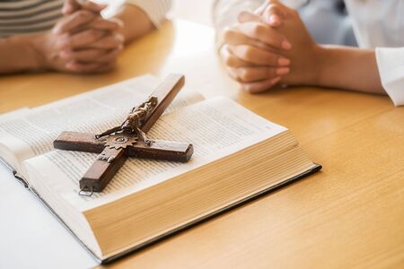 Christian woman praying with hands together on holy bible and wooden cross. Woman pray for god...