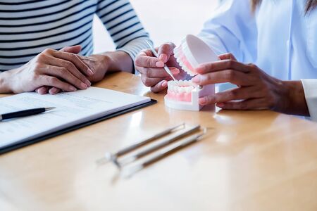 Dentist showing and explaining teeth disease treatment to patient using teeth model denture and...