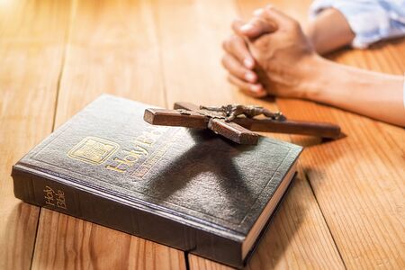 Christian woman praying with hands together on holy bible and wooden cross. Woman pray for god blessing to wishing have a better life and believe in goodness.の写真素材