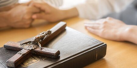 Christian woman praying with hands together on holy bible and wooden cross. Woman pray for god...
