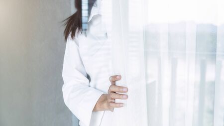 Asian woman opening window blinds after get up in morning sunrise. Morning lifestyle concept.の写真素材