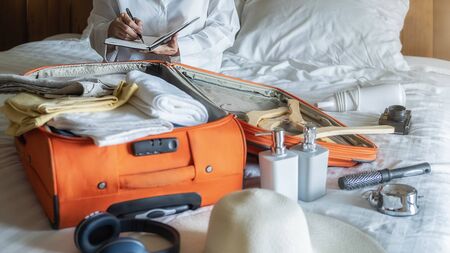 Preparation for vacation or travel. Happiness young woman packing a clothes and stuff into opened suitcase on bed.の写真素材
