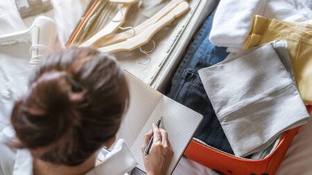 Preparation for vacation or travel. Happiness young woman packing a clothes and stuff into opened...